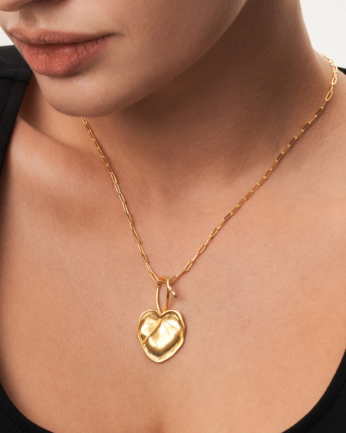 a woman wearing a necklace with a heart shaped pendant